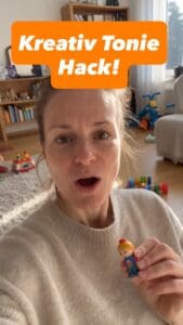 Frau zeigt kreativen Tonie Hack mit Spielzeugfigur in Wohnzimmer.